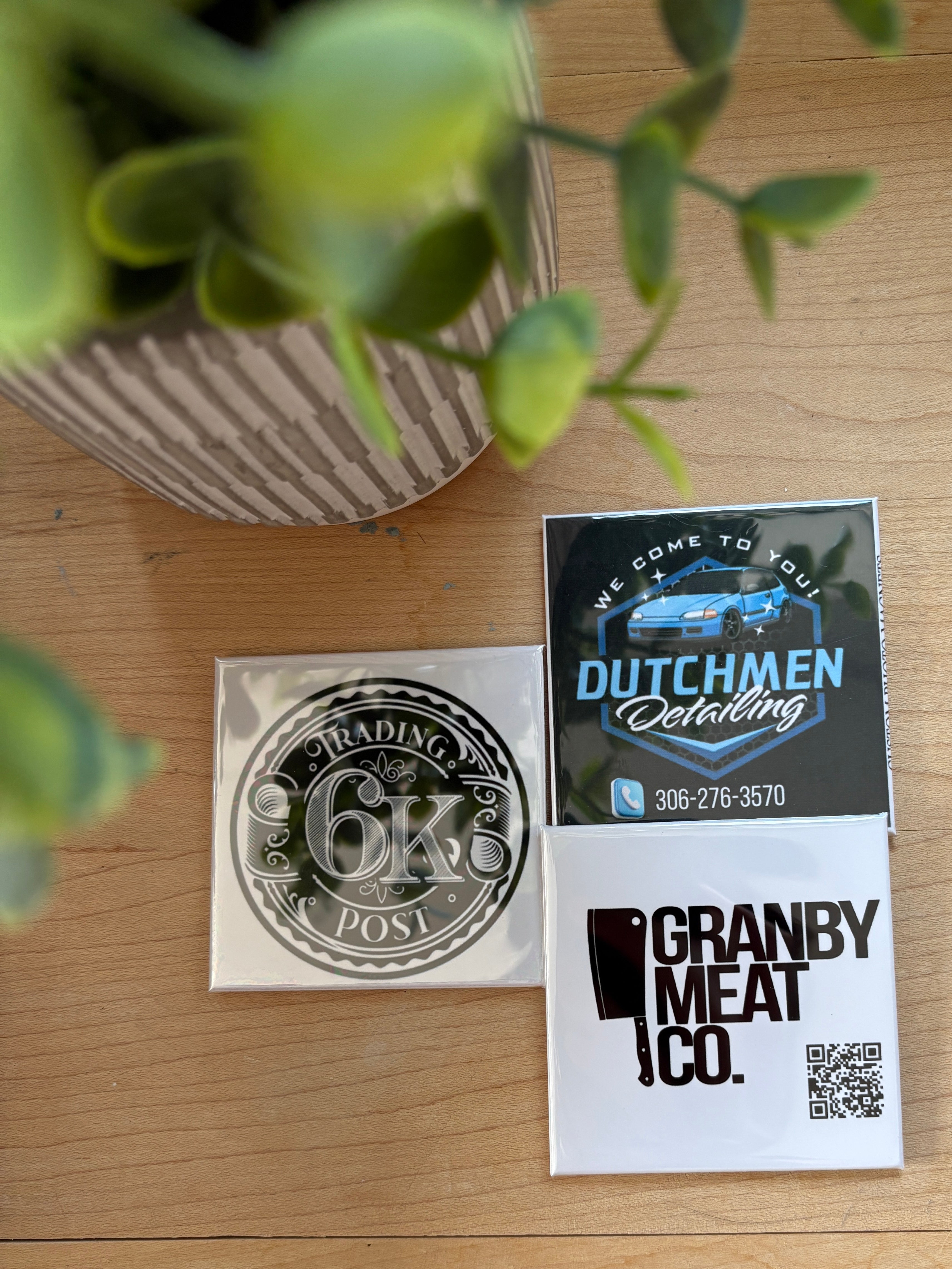 Three business cards on a wooden surface with a plant in the foreground